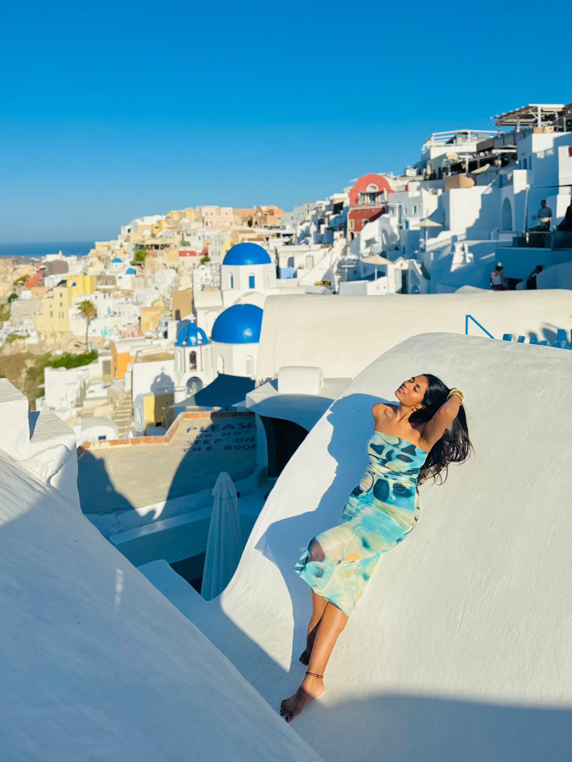 Strapless tube dress with pastel tie-dye patch print in blues and greens, worn by a woman on white Santorini stairs.