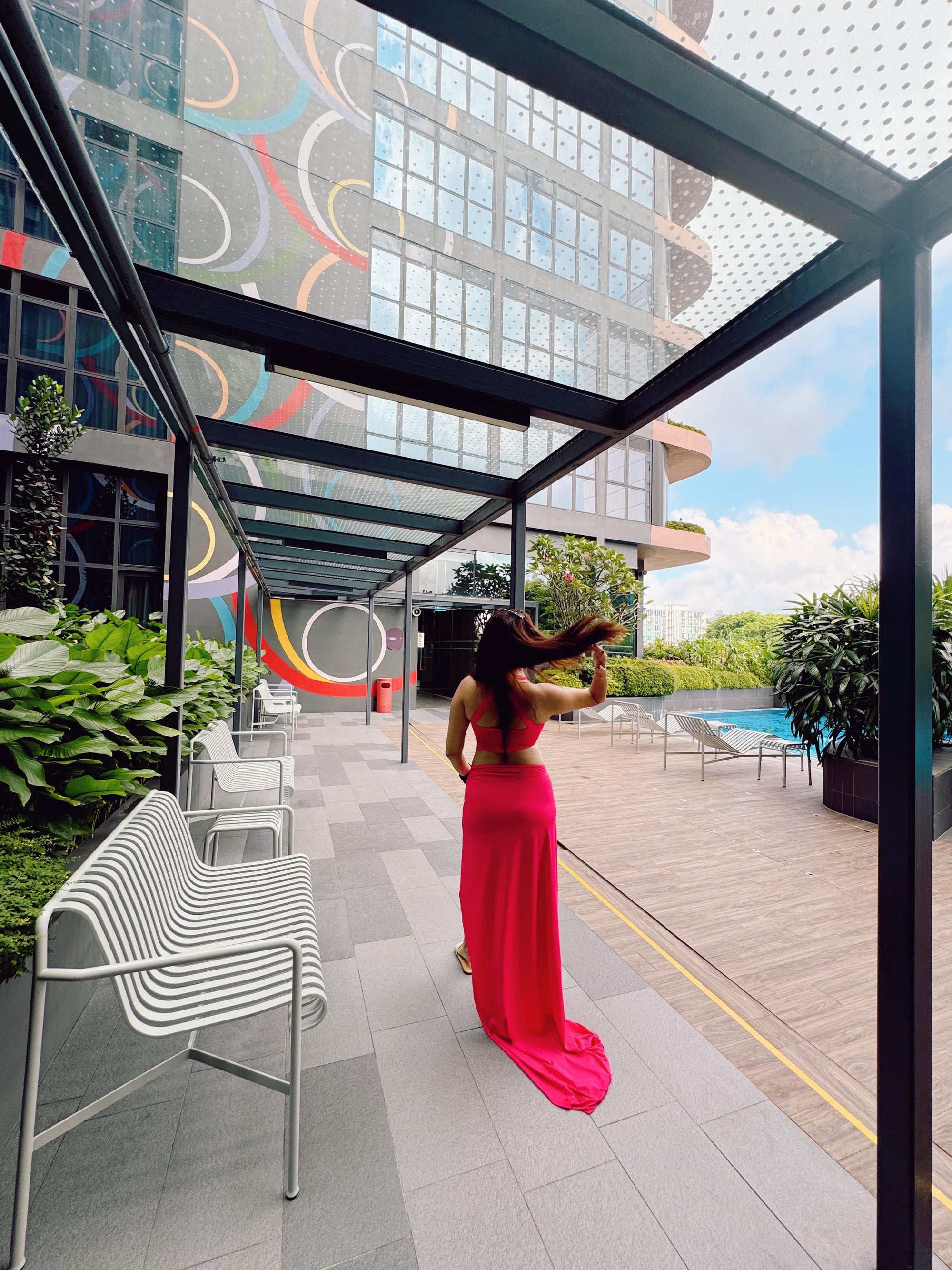 Back view of a woman in a bright pink cutout cropped tank top and matching high-waisted skirt, by a pool.