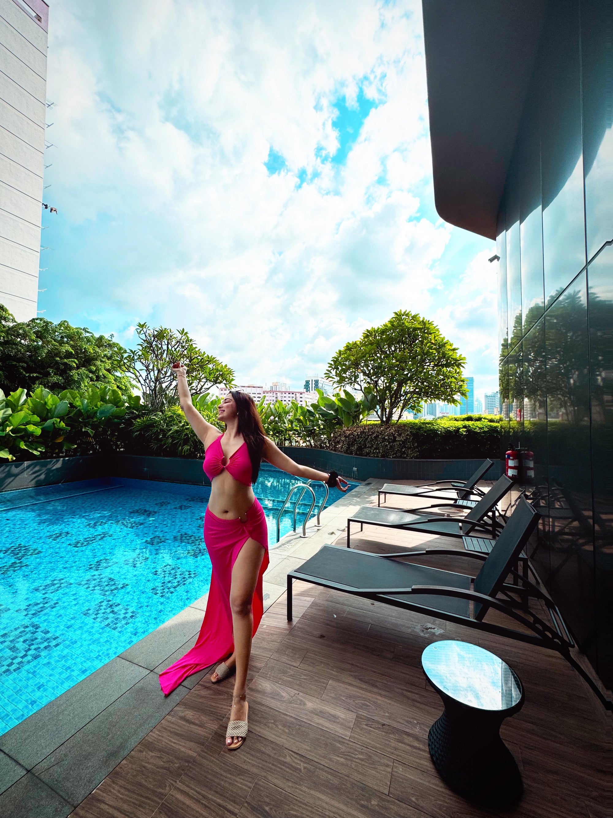 Woman in hot-pink cutout cropped tank top and high-waisted skirt with thigh-high slit, poolside posing.