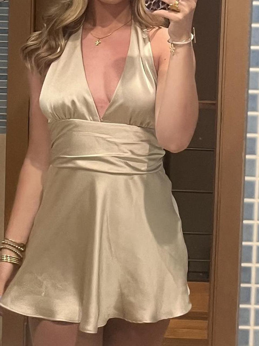Cream satin halter-neck dress with a deep neckline, wrapped waist, and flared A-line skirt; gold bracelets.