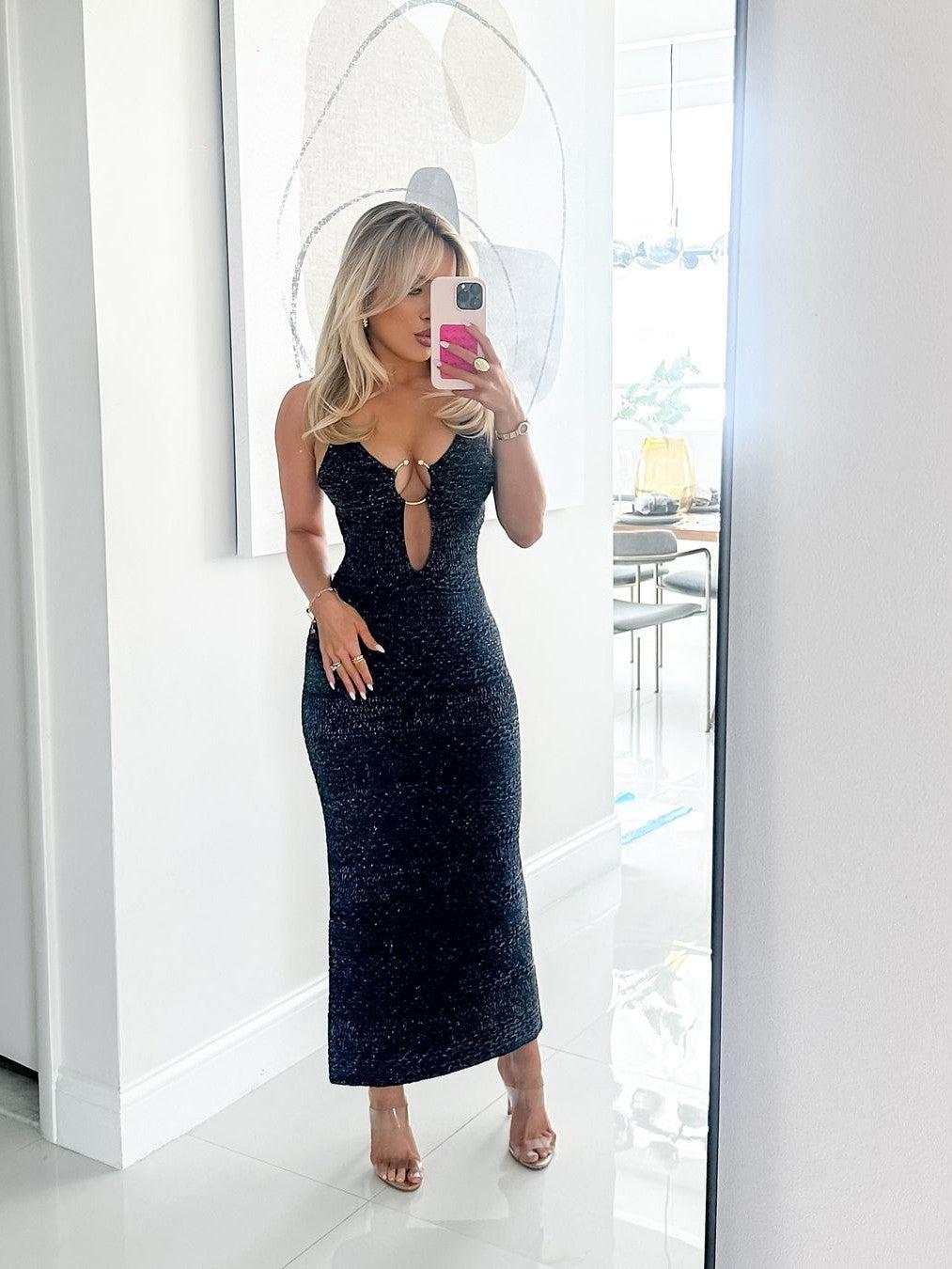 Blonde in a black speckled knit spaghetti-strap dress with a front keyhole cutout and ring detail, midi length.