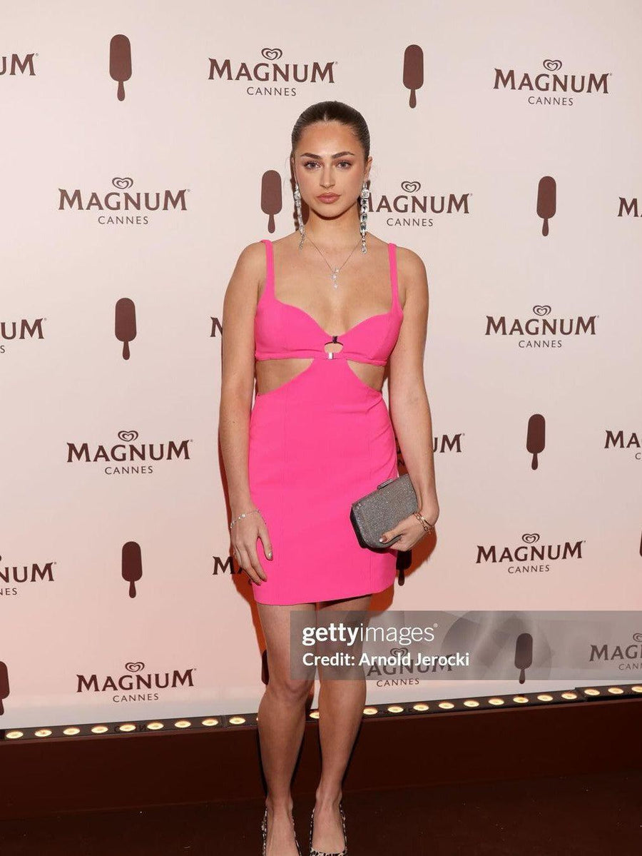 Bright pink spaghetti-strap mini dress with front ring detail and side cutouts, worn on red carpet with a silver clutch