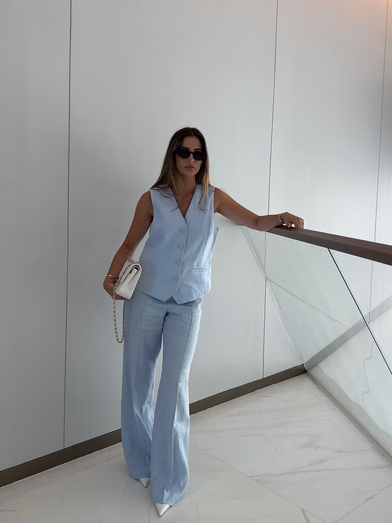 Light blue sleeveless waistcoat with matching wide-leg pants, worn with sunglasses and a white chain bag indoors.