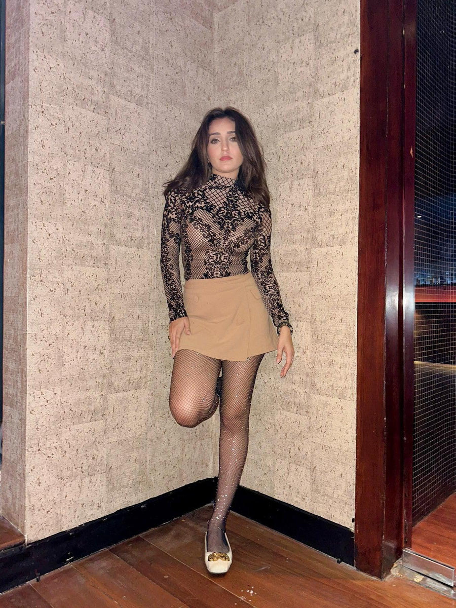 Model in black high-neck lace mesh bodysuit with nude lining, beige mini skirt, glittery tights.