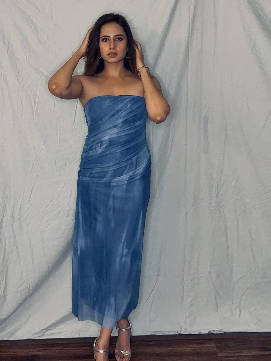 Woman in a blue tie-dye strapless mesh tube dress with ruched wrap, posing against a light backdrop in silver sandals.