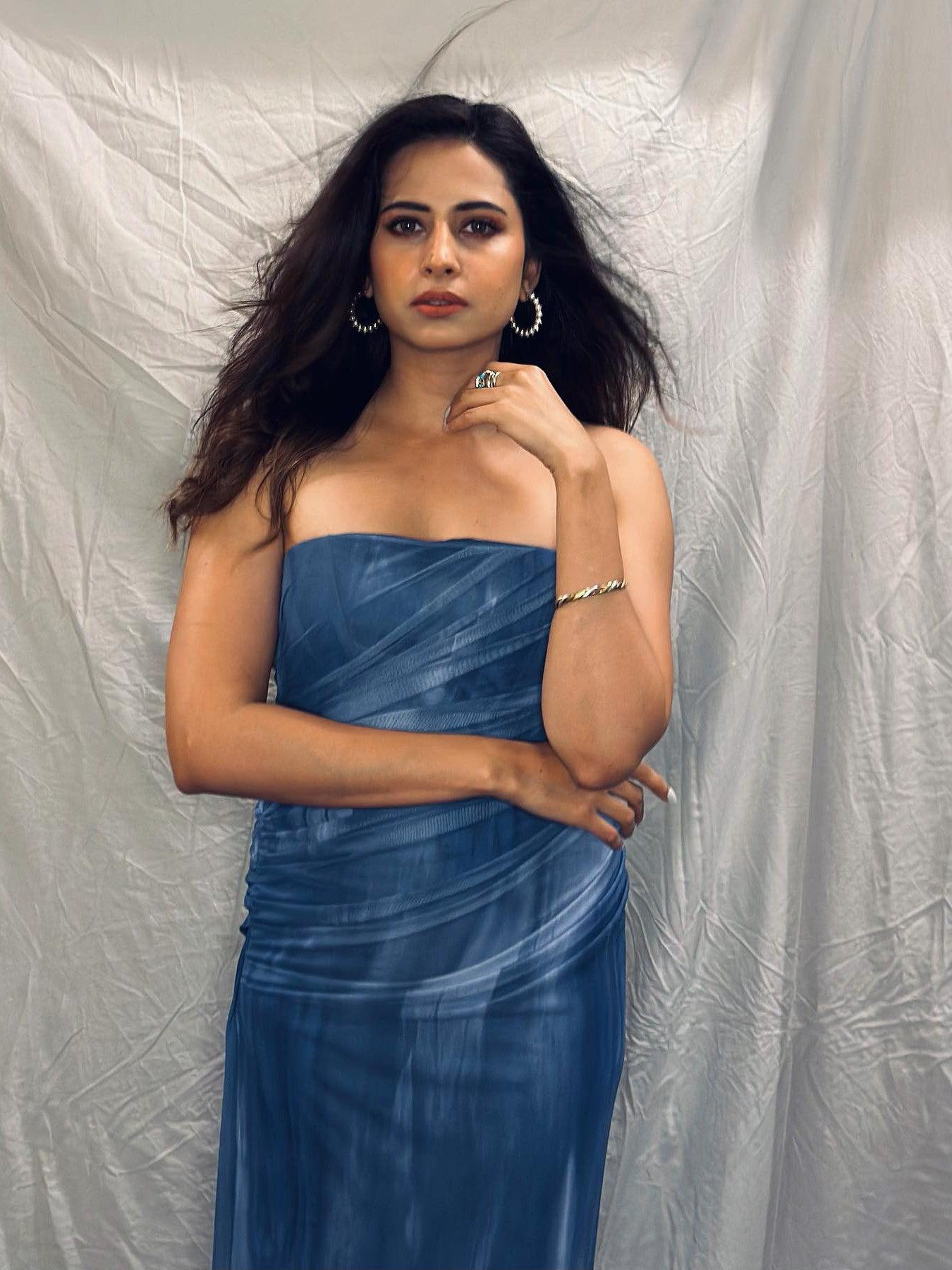 Model wearing strapless blue tie-dye mesh tube dress with draped ruching, against a light backdrop; hoop earrings.