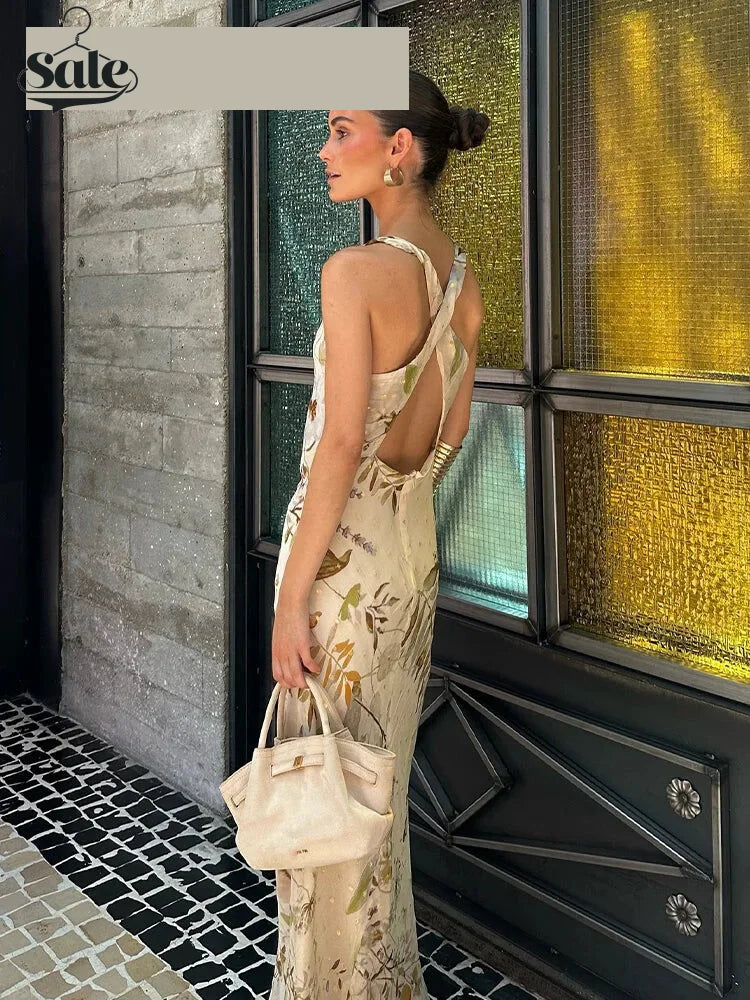 Cream floral printed cowl-neck fit-and-flare maxi dress with crossback cutout; model holds beige handbag by a glass storefront