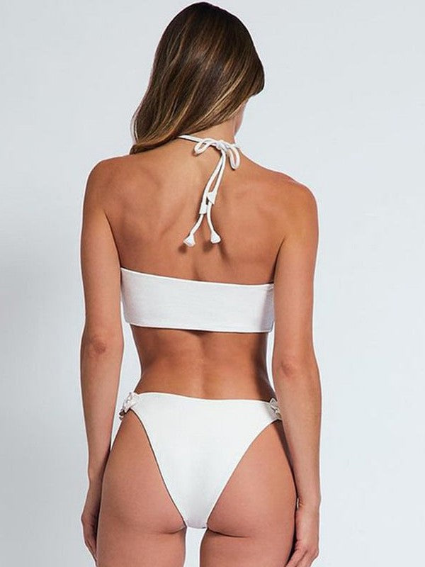 Back view of white bikini: halter-tie bandeau top, straps tied behind neck, bottom with floral appliques at the hips.