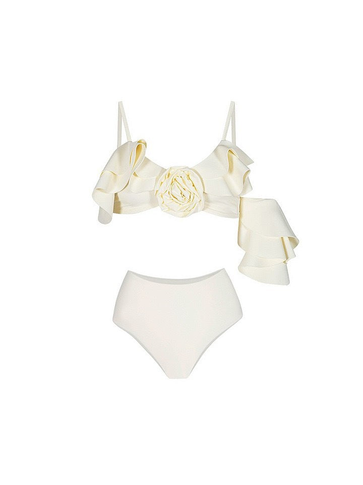 Ivory bikini with a large 3D rose at the center, cascading asymmetric ruffles and a flutter sleeve; high-waisted bottom.