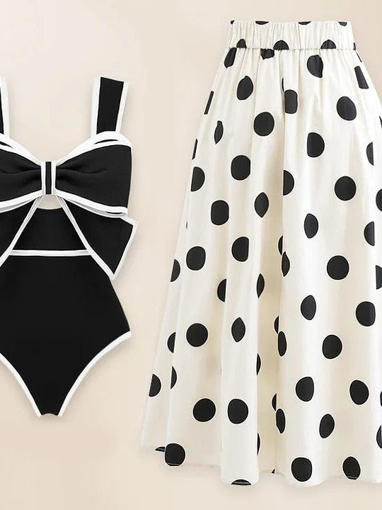 Black one-piece swimsuit with white piping and a large bow, paired with a white chiffon skirt with big black polka dots.