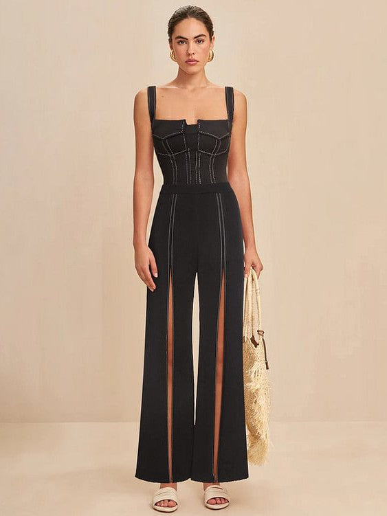 Woman in black corset-style top and high-waisted wide-leg pants with sheer panels, holding a fringed straw bag.