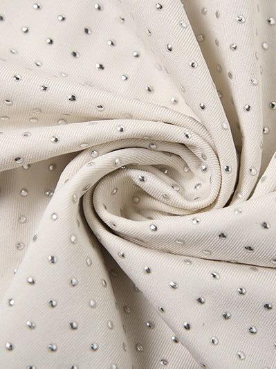 Close-up of beige textured fabric dotted with tiny silver rhinestones, twisted into a spiral.