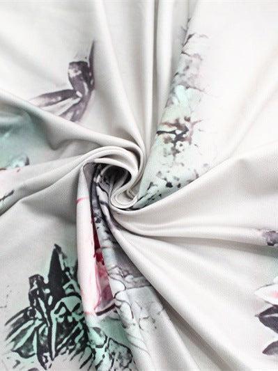 Light-gray satin fabric with pastel floral print, twisted into a spiral to reveal soft folds and sheen.