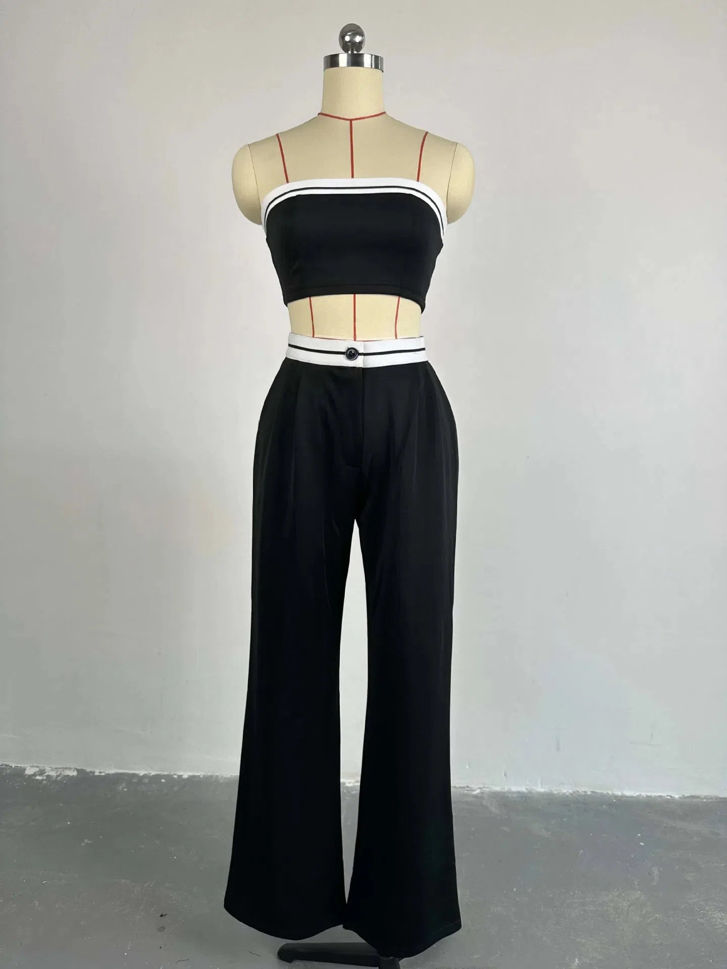Black bandeau top with white striped trim, paired with black wide-leg pants and a white belt with a black button.