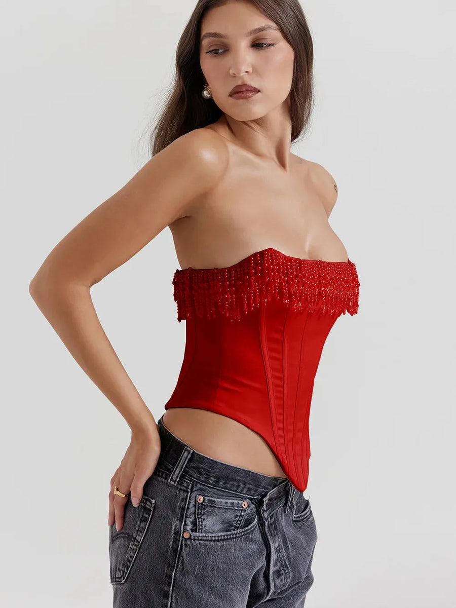 Red strapless corset top with beaded fringe trim and boned satin panels, model wearing dark denim jeans.