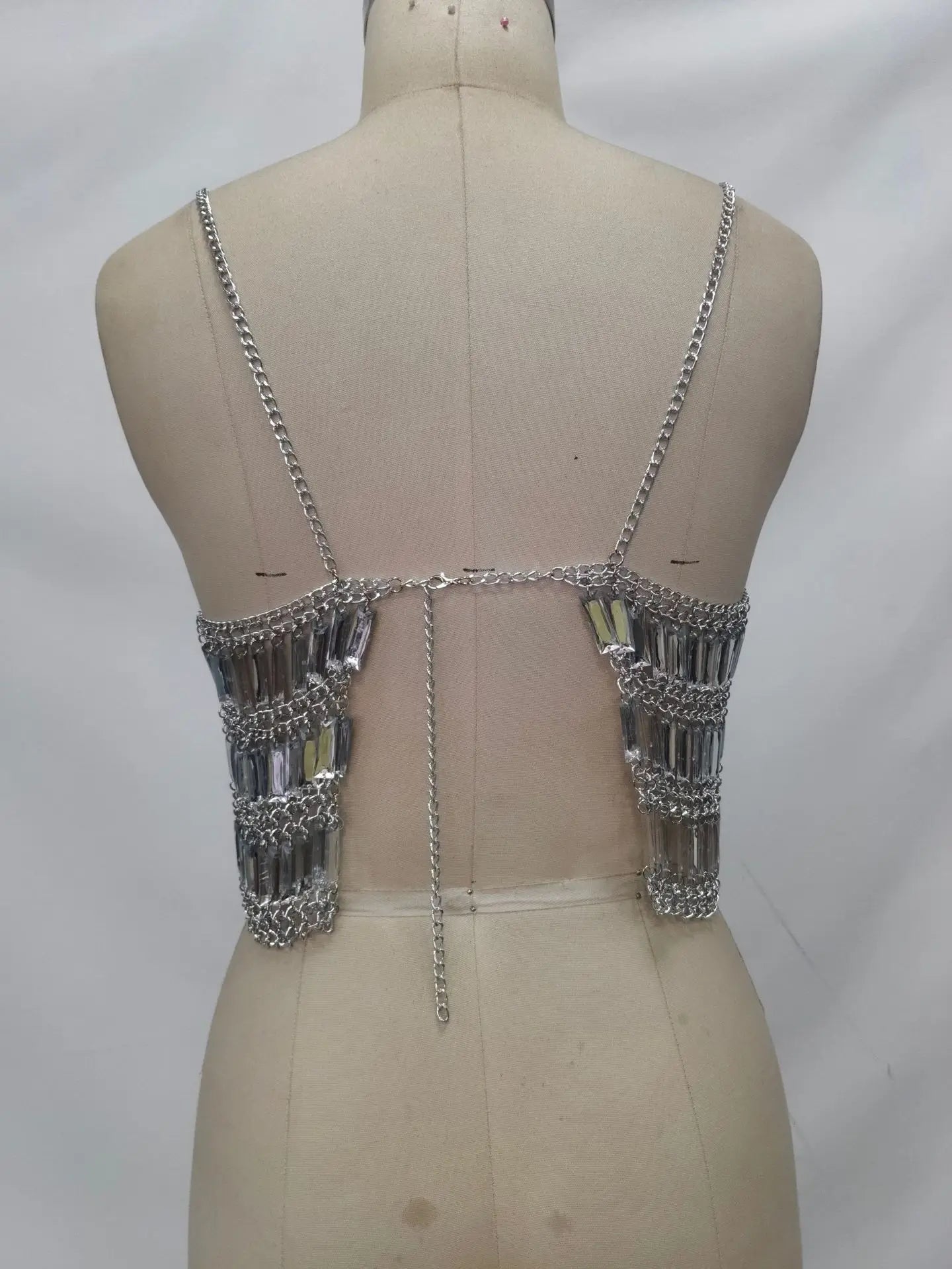 Back view: silver chain bralette with crystal fringe panels on both sides and a central dangling chain, on a dress form.