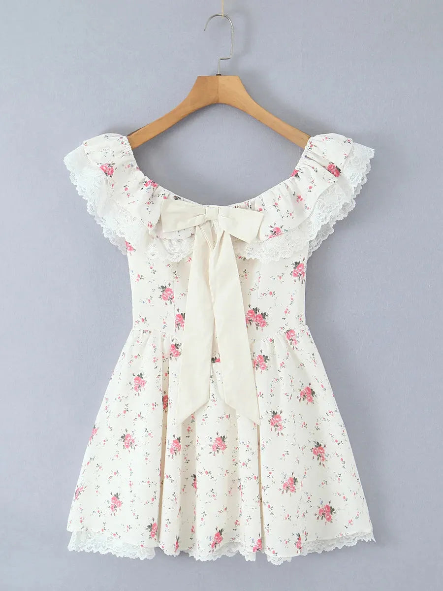 Ivory off-shoulder mini dress with lace-trimmed ruffles, lace hem, cream bow at front, pink rose print, on a hanger.