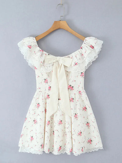Ivory off-shoulder mini dress with lace-trimmed ruffles, lace hem, cream bow at front, pink rose print, on a hanger.