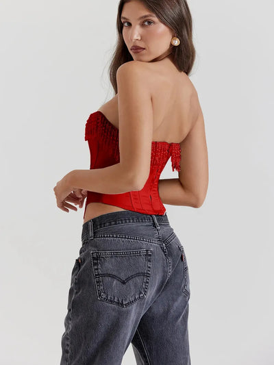 Red strapless corset top with bead-embellished fringe along the bust, boning panels, shown on a model with dark jeans.