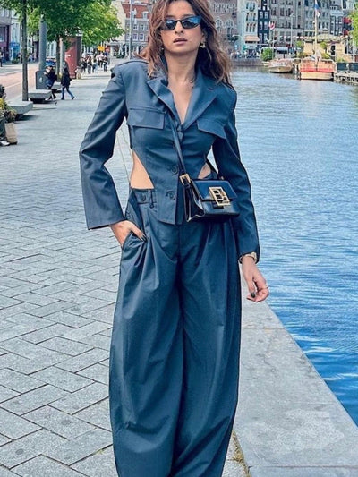 Teal satin-like blazer with waist cutouts and matching wide-leg pants; woman with black crossbody bag and sunglasses.