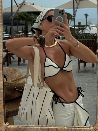 Poolside woman in a white triangle bikini with black piping and tie sides, paired with a white sarong with black trim.