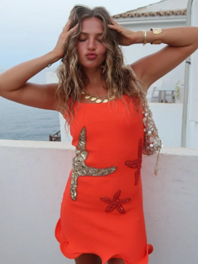 Bright orange mini dress with silver and red starfish sequin patches, one sheer beaded sleeve, ruffled hem.