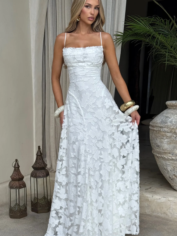 Model wearing white floral appliqué cowl-neck A-line maxi dress with spaghetti straps, outdoors near lanterns.