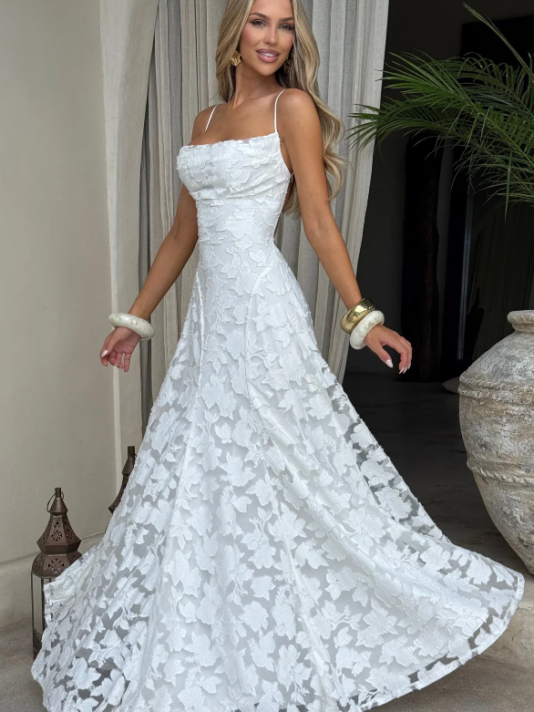 Woman wearing a white floral appliqué cowl-neck A-line maxi dress with thin spaghetti straps, posing indoors.