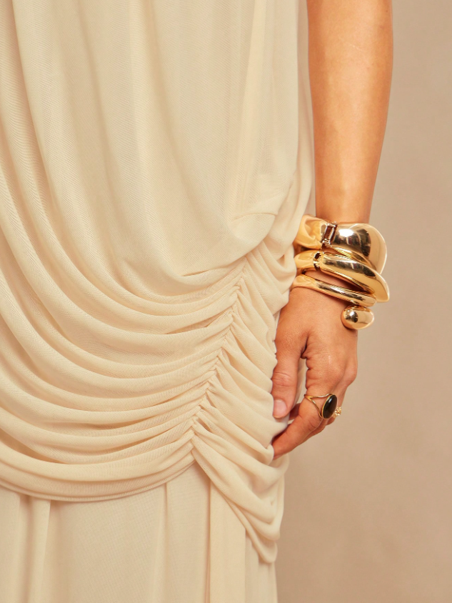 Ivory draped fabric with side ruching on a strapless dress, hand wearing chunky gold bracelets and ring.