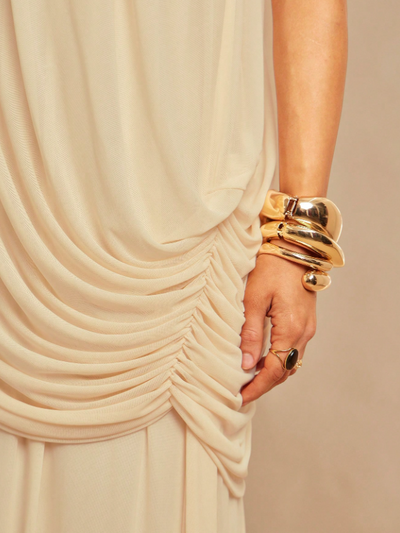 Ivory draped fabric with side ruching on a strapless dress, hand wearing chunky gold bracelets and ring.