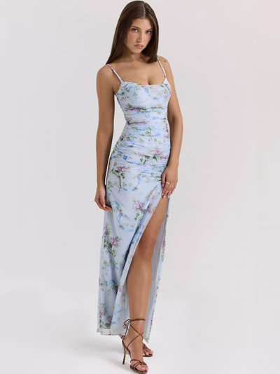 Model wearing sky-blue floral ruched maxi dress with spaghetti straps and high thigh slit, white studio backdrop.