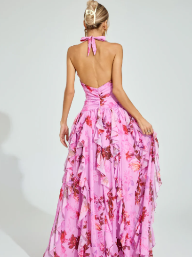 Back view of woman in pink floral halter maxi dress with open back, pink neck tie, and layered ruffled skirt.