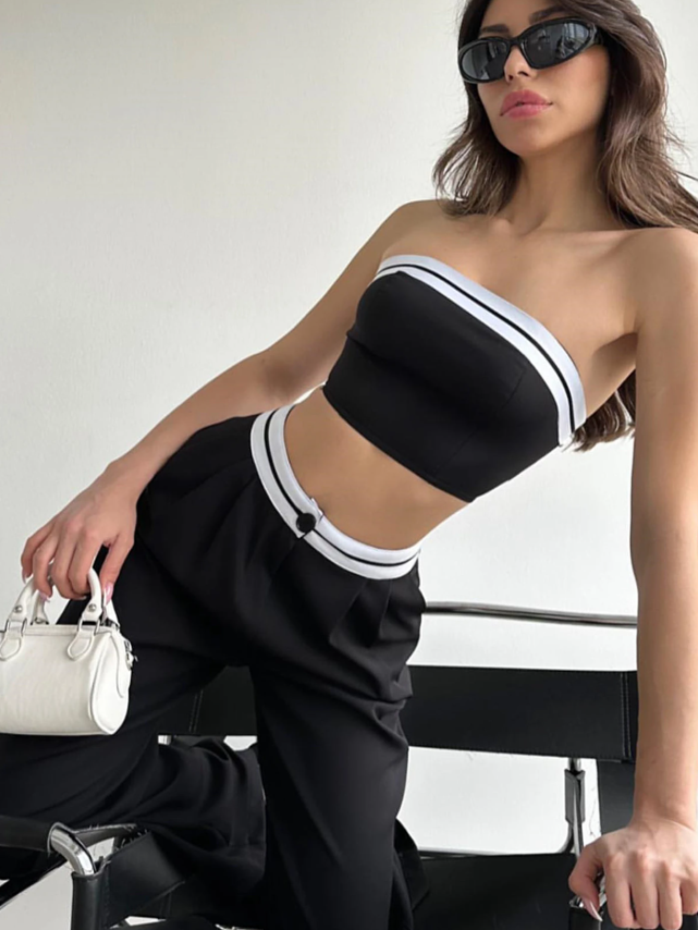 Woman in black tube top with white striped trim and matching wide-leg pants, white belt, sunglasses, and white handbag.