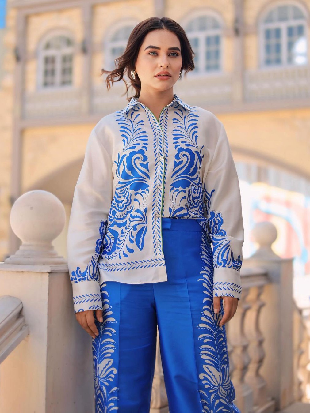 Woman in a white buttoned shirt with blue porcelain floral print and blue pants with side panels, outdoors.