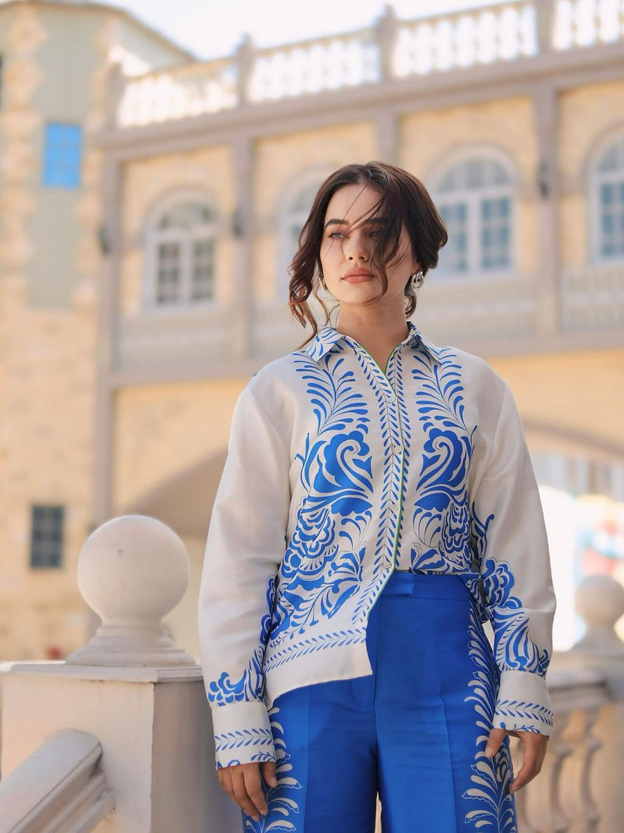 Woman wearing a white shirt with blue porcelain print and cobalt blue pants, outdoors beside a balustrade.