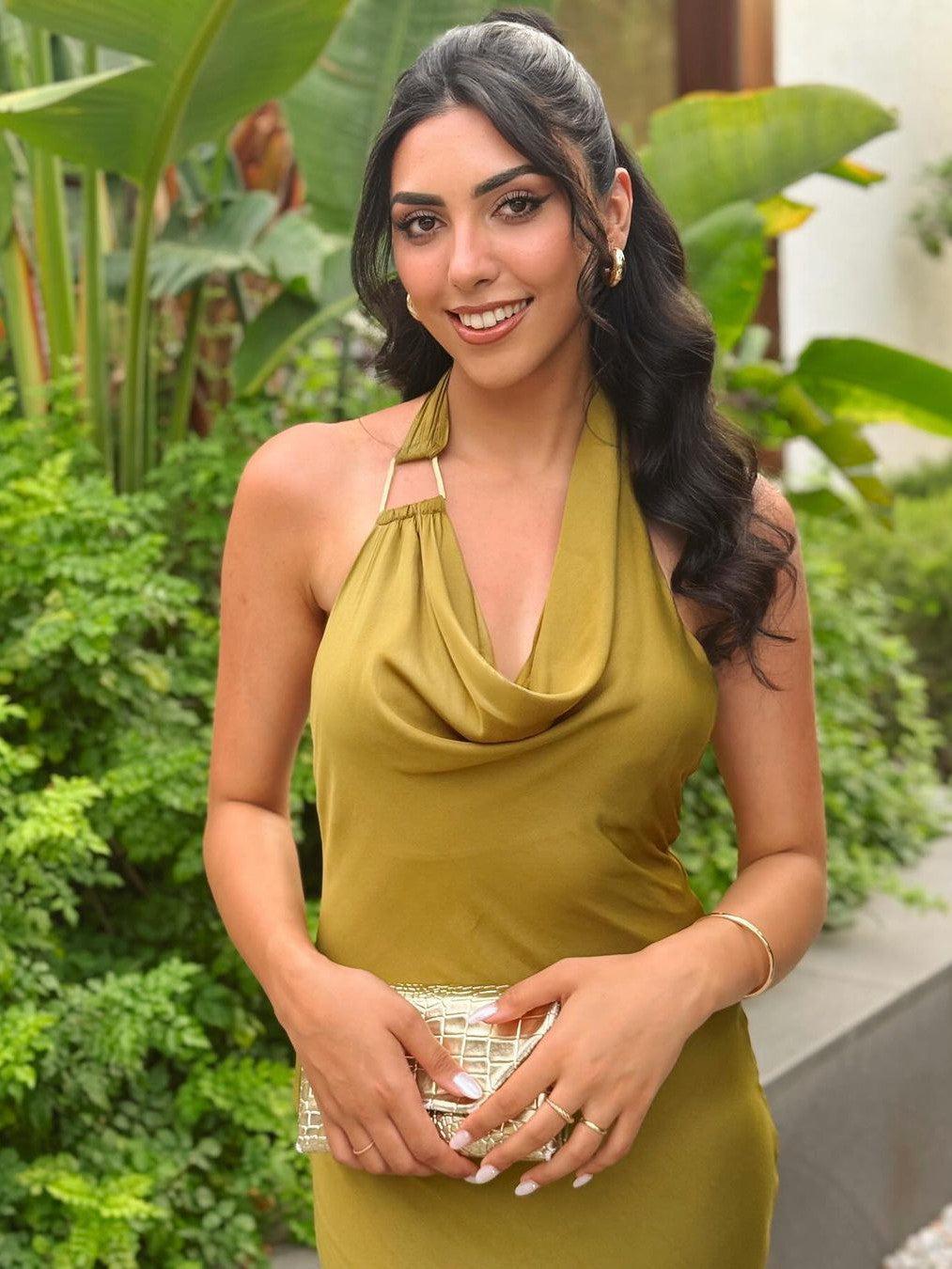 Olive satin-blend halter maxi dress with draped cowl neckline, worn by woman holding a gold quilted clutch in a garden.