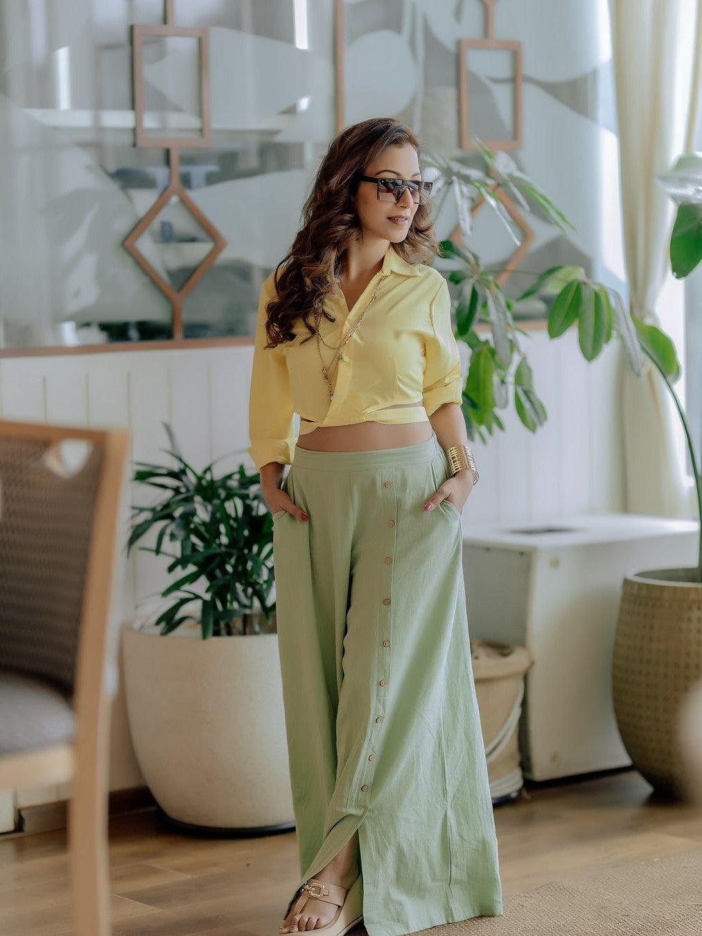 Woman in a yellow cropped button-down top and mint green linen wide-leg pants with a buttoned front.