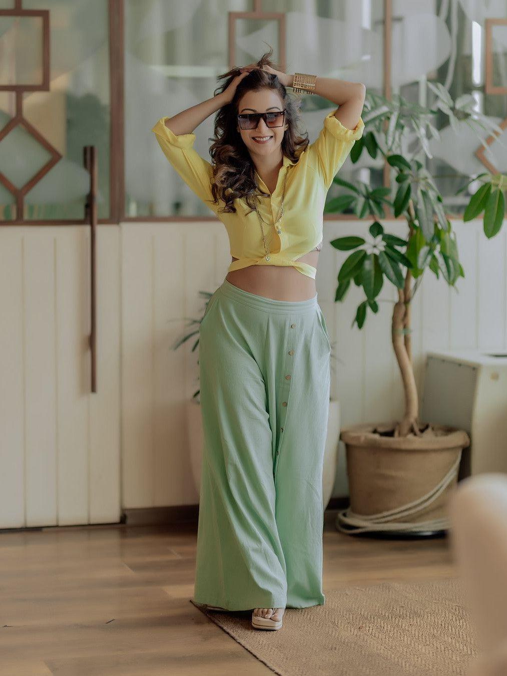 Woman in a yellow cropped blouse with long sleeves and mint-green linen wide-leg pants, posing indoors with sunglasses.