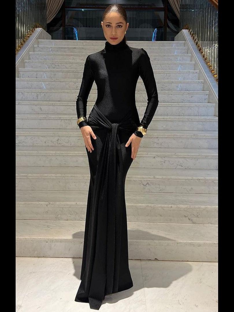 Model in black high-collar knot-front full-sleeve maxi dress with waist knot, on marble stairs.