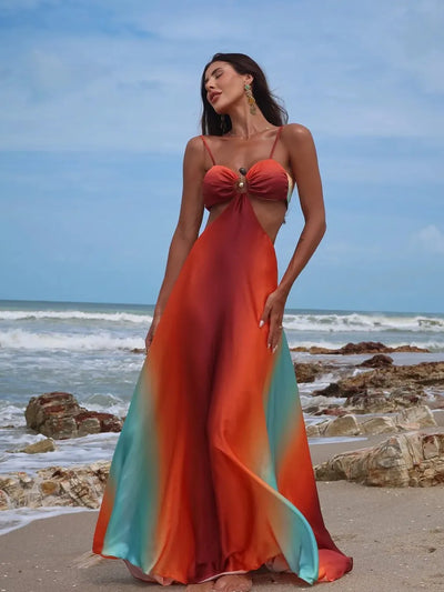 Beach model in gradient tie-dye cutout maxi dress with red-orange top, center ring, thin straps, and teal panels.