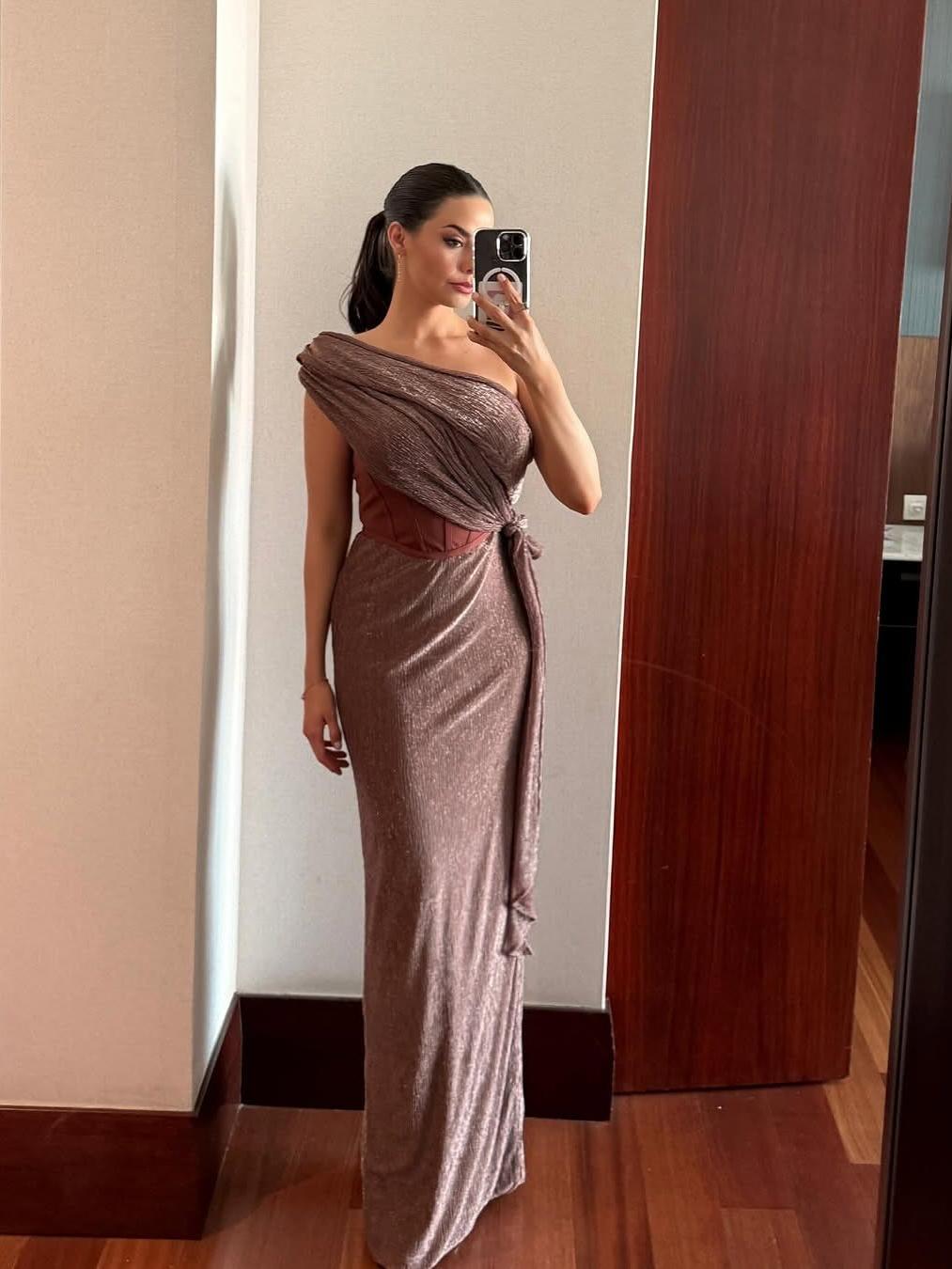 Mirror selfie of a woman in rose-gold shimmery draped off-shoulder gown with a brown corset belt and side tie.
