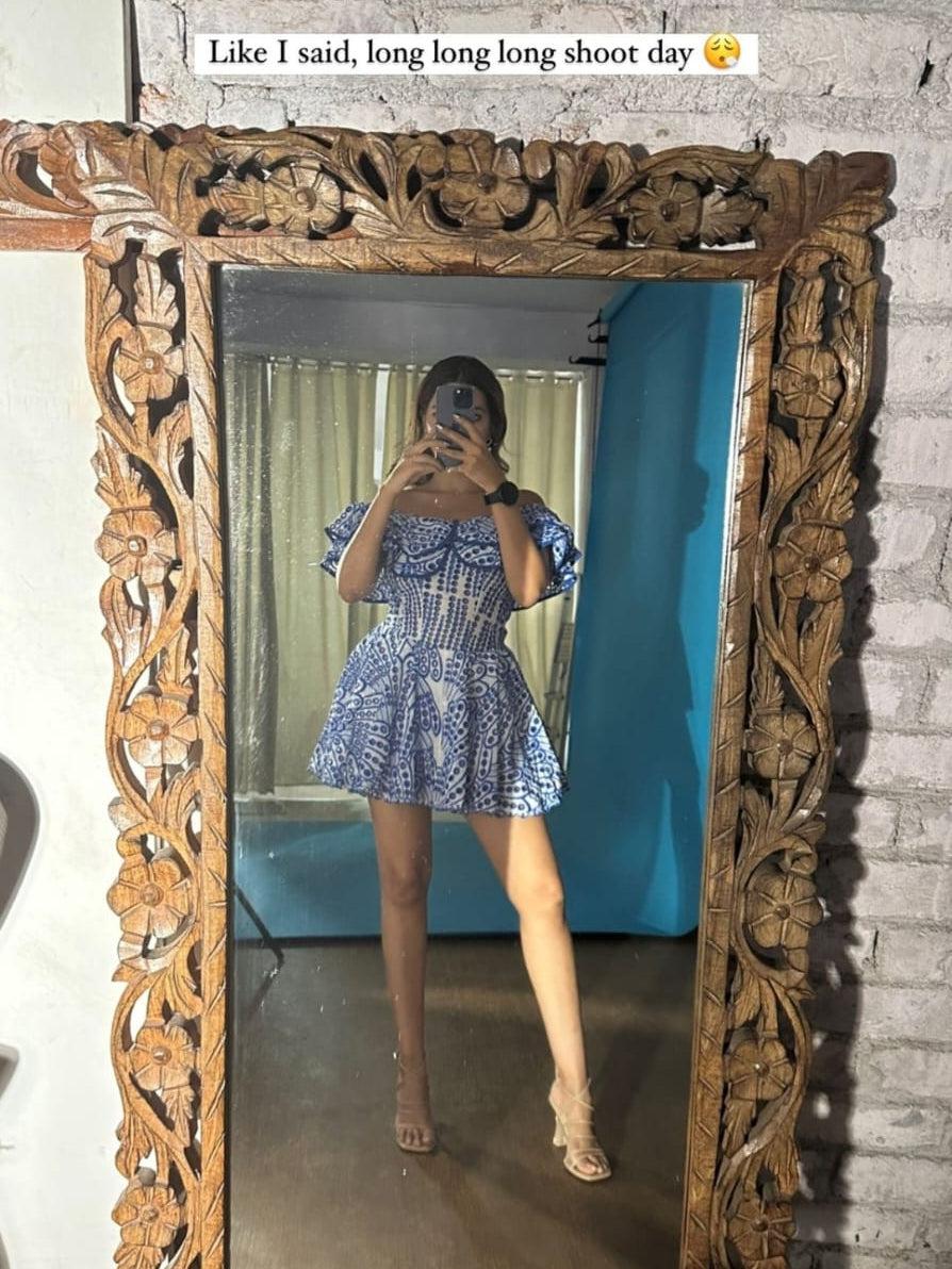Blue and white off-shoulder short embroidered dress with a smocked bodice and flared skirt, model posing in a mirror.