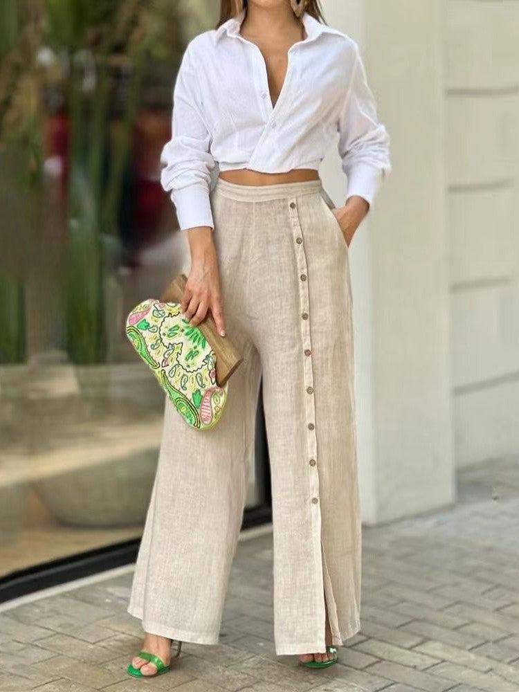 White cropped shirt tied at the waist with beige linen wide-leg pants; front button row, clutch in hand, green sandals.