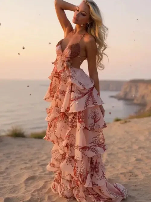 Blush pink butterfly-print tiered ruffle maxi dress with thin straps, worn by a model on a beach at sunset.
