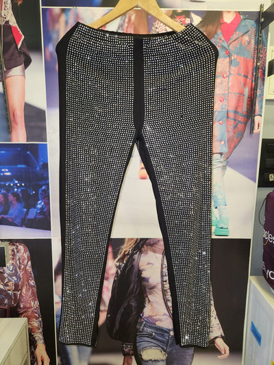 Black full-length pants covered in silver rhinestones, straight-leg fit, hung on a wooden hanger in a store.