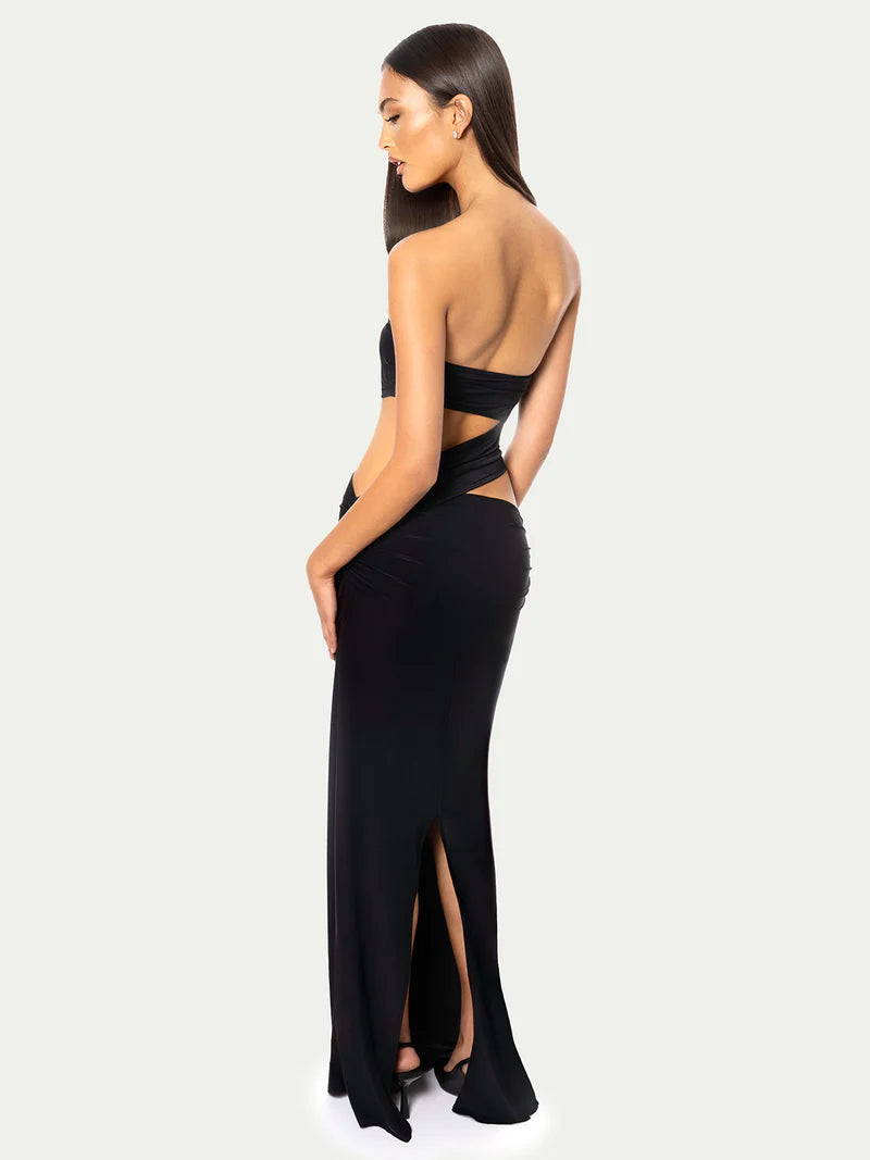 Back view of a model wearing a black strapless cut-out bodycon maxi dress with waist openings and a thigh-high slit