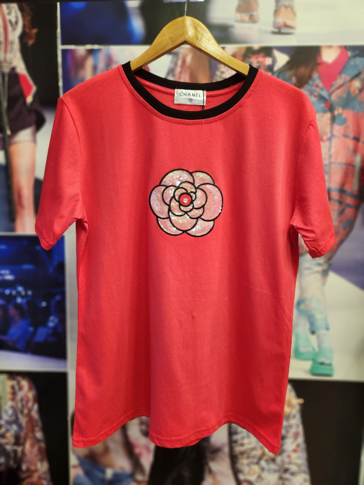 Coral pink cotton-lycra T-shirt on a wooden hanger, black crew-neck trim, pink sequined flower applique on chest.