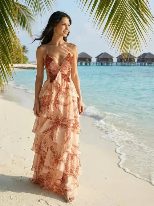 Woman on a beach wearing a blush butterfly-print tiered ruffle maxi dress with spaghetti straps and a front bow.