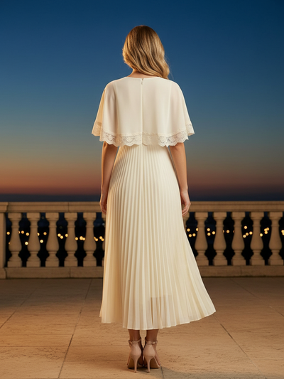 Back view of ivory cape-sleeve maxi dress with lace trim and pleated skirt, standing on a terrace at sunset.
