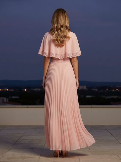 Back view of pale pink pleated maxi dress with lace-trim capelet and fitted waist on a rooftop at dusk